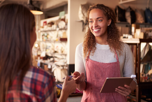 Smiling woman with tablet assists customer in eclectic shop - Setting up a business
