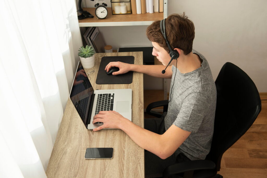 Person using a laptop with a headset at a home desk for online work or communication.