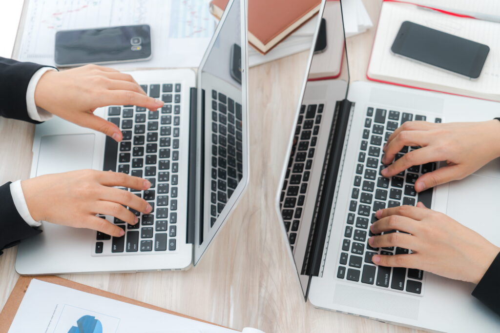 Aerial view of two business professionals working on laptops at a shared desk, with financial charts and documents visible