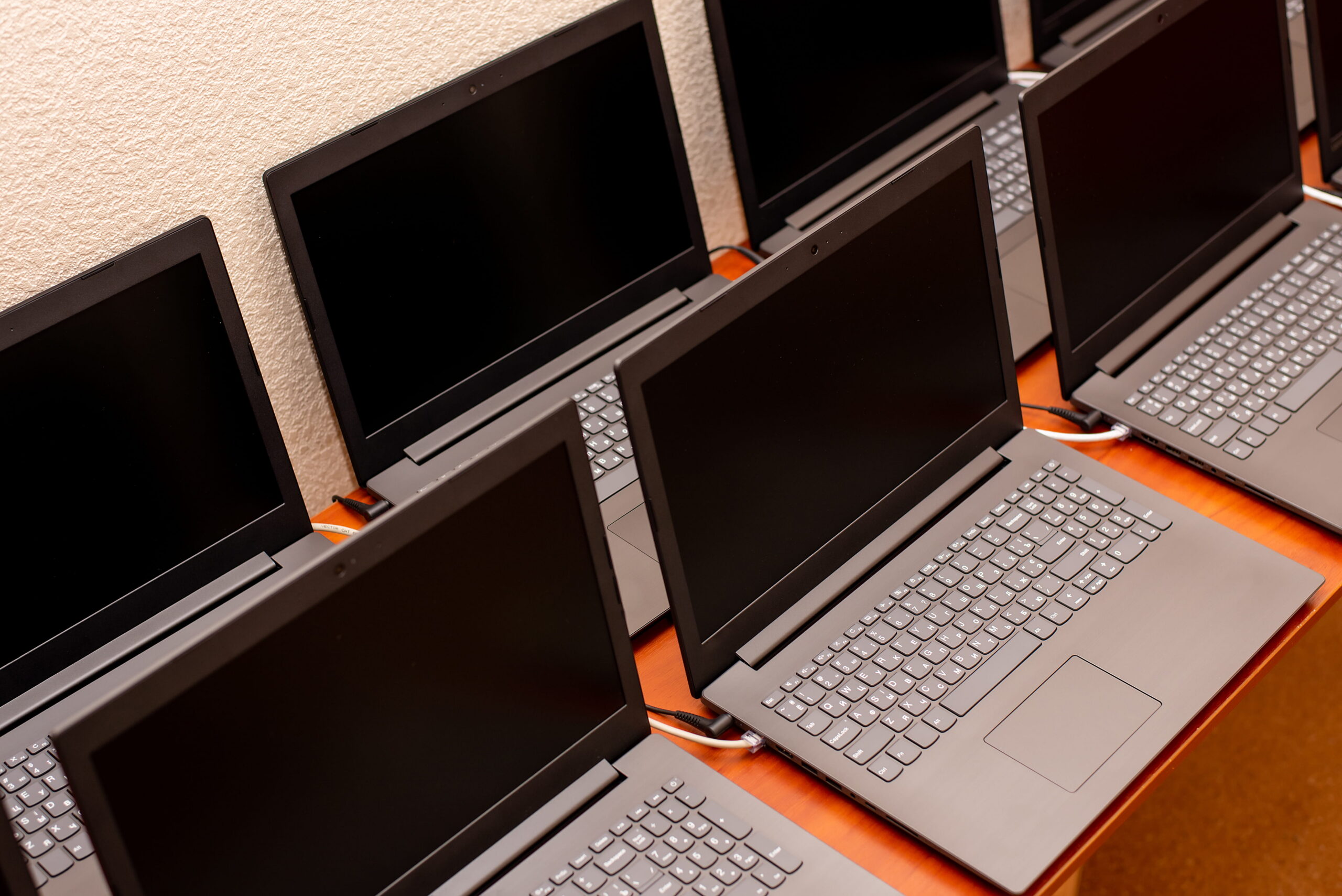 Multiple identical laptops with blank screens arranged in close rows on a table for a technology demonstration