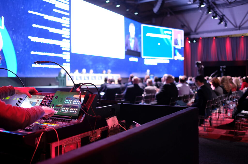 AV technician operating a control desk during a large conference with multiple screens