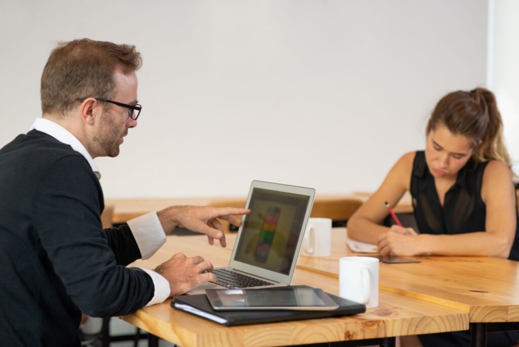 Two business professionals reviewing a MacBook rental decision at a desk.