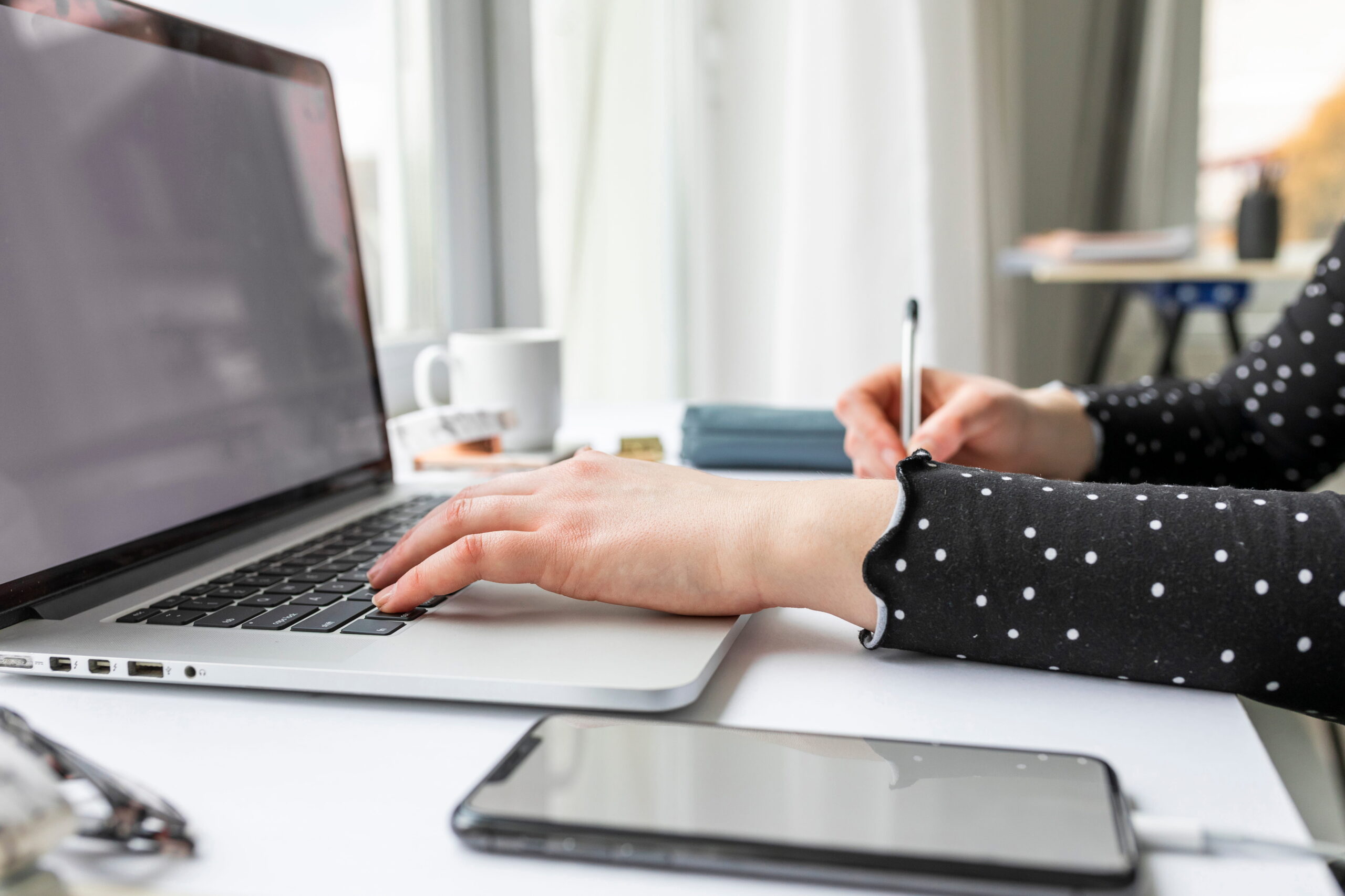 A businesswoman working on an Apple MacBook while taking notes.